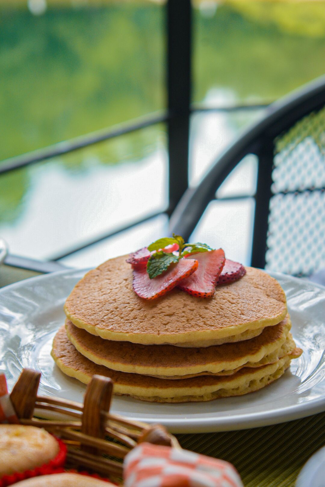 Una pila de panqueques con fresas encima en un plato blanco.
