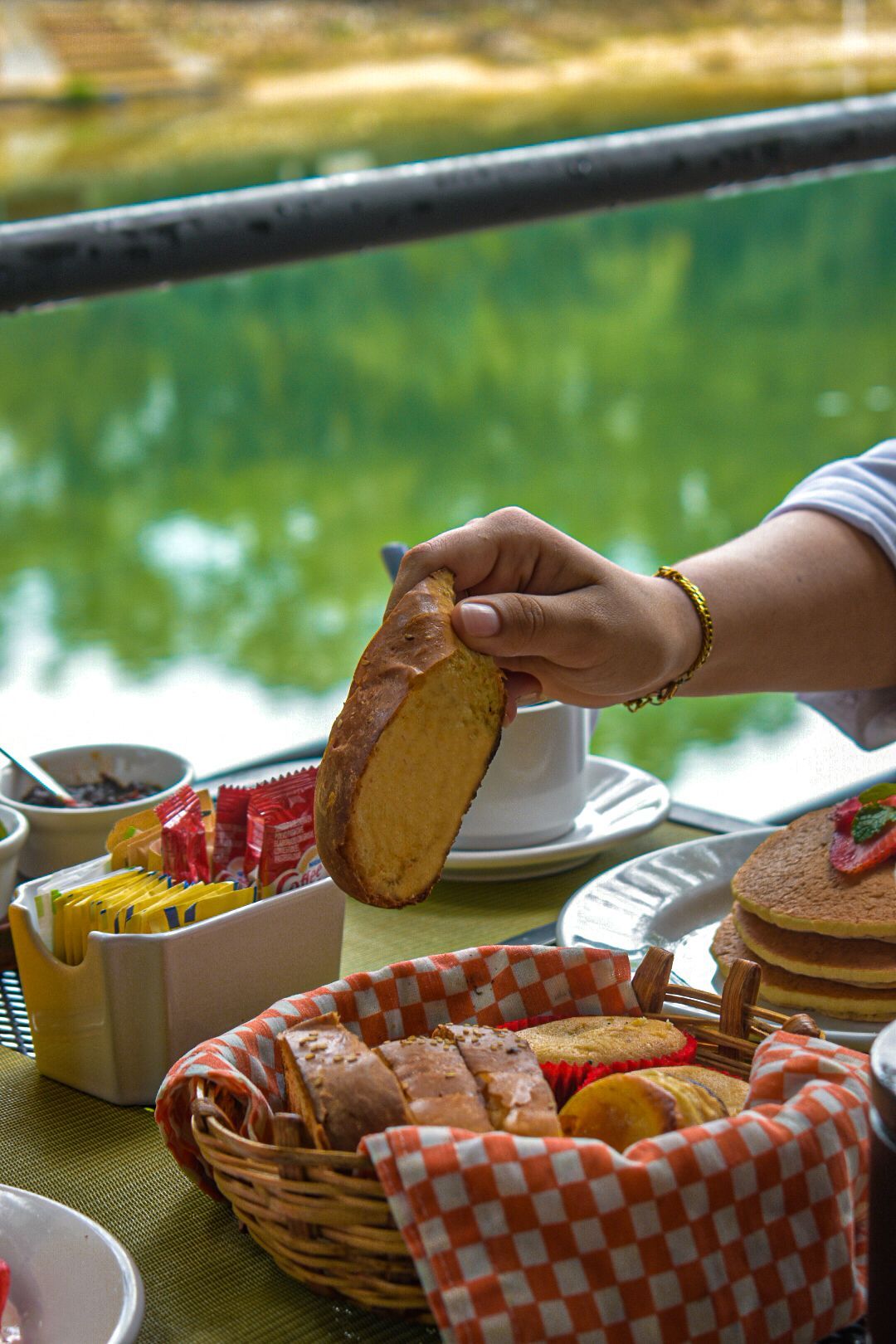 Una persona sostiene un trozo de pan sobre una canasta de comida en una mesa.