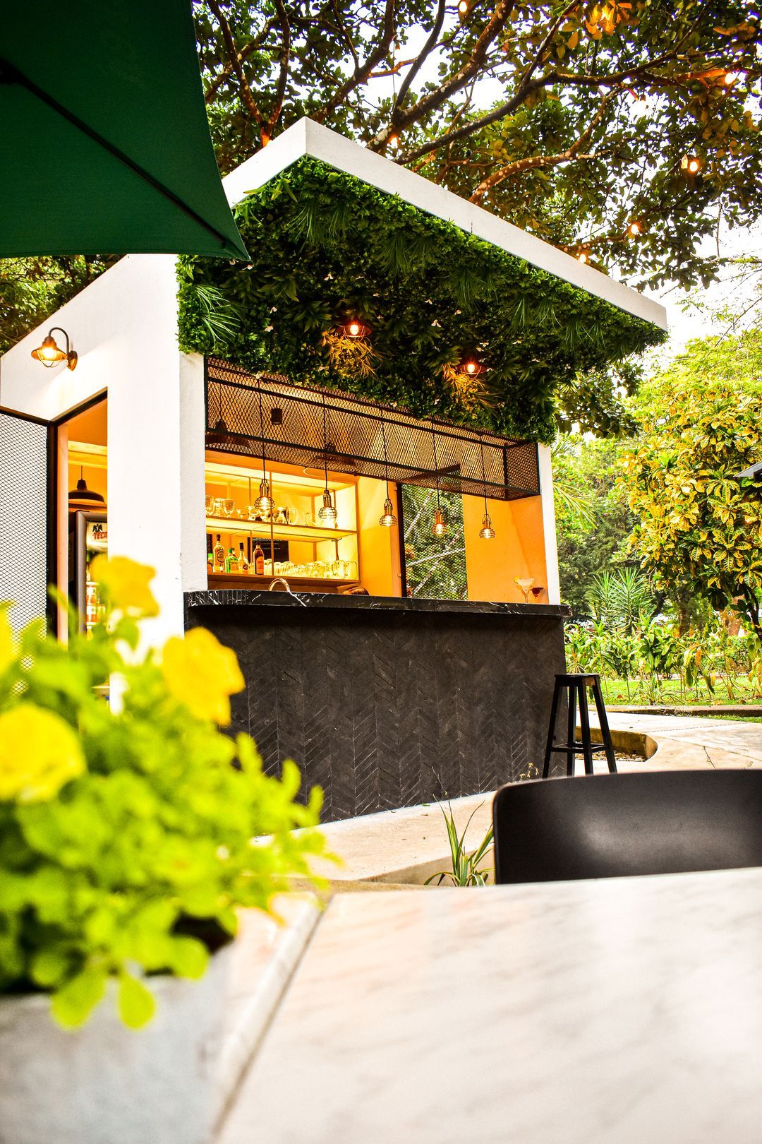 Un bar con una sombrilla verde y flores delante.