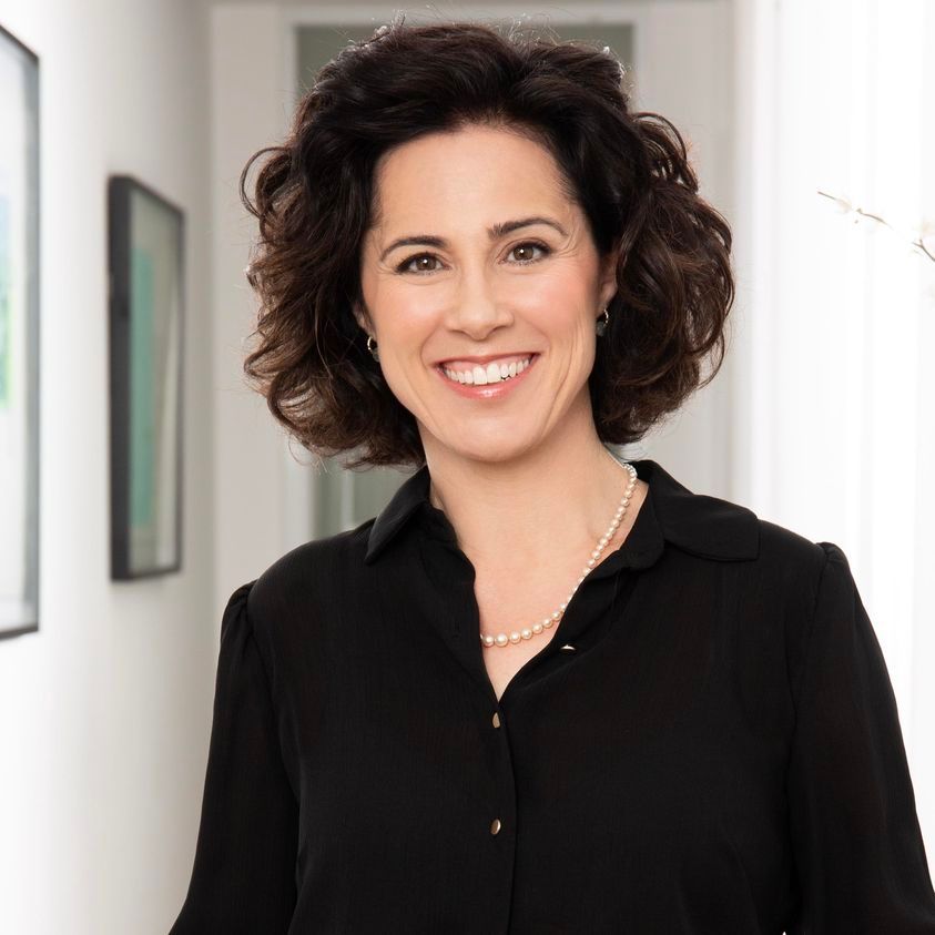 אישה לובשת חולצה שחורה ושרשרת פנינים מחייכת למצלמה