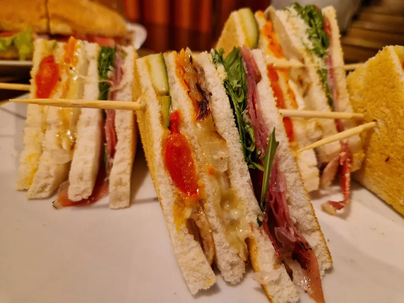 Panini triangolari su un piatto bianco, tenuti insieme da stuzzicadenti. Contenuto visibile: carne, verdure e salsa.