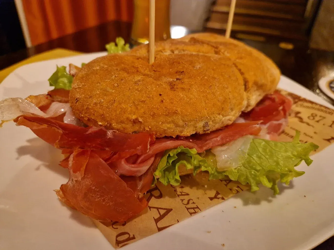 Panino con prosciutto, lattuga e pane, tenuti insieme da stuzzicadenti, su carta.