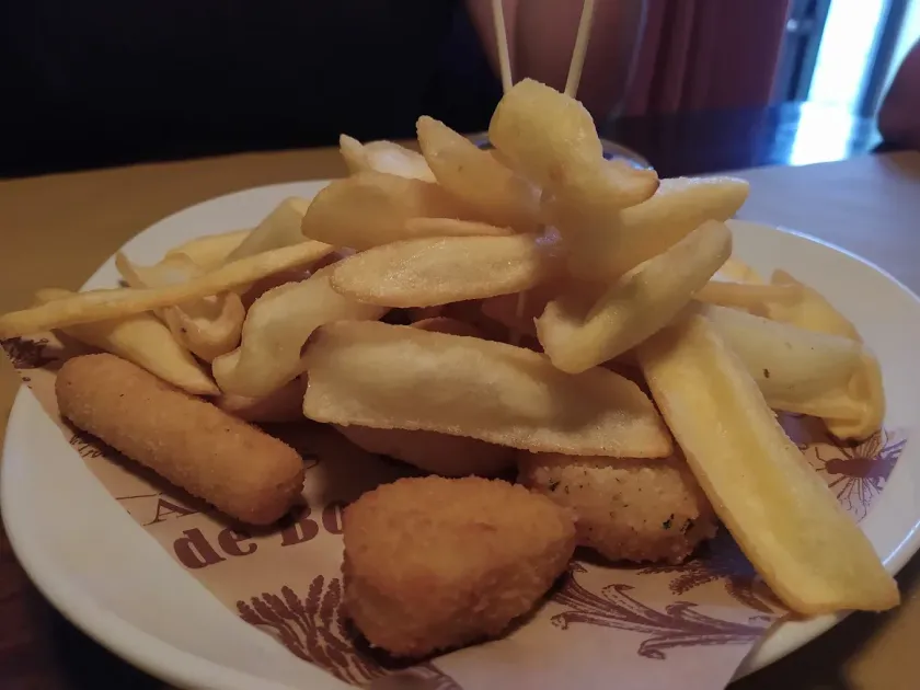 Piatto di patate fritte, bastoncini di formaggio e un cubo impanato su un piatto bianco con carta fantasia.