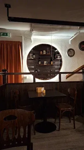 Accogliente ristorante interno con sedie in legno, un tavolo scuro e uno scaffale espositivo circolare illuminato sul retro.