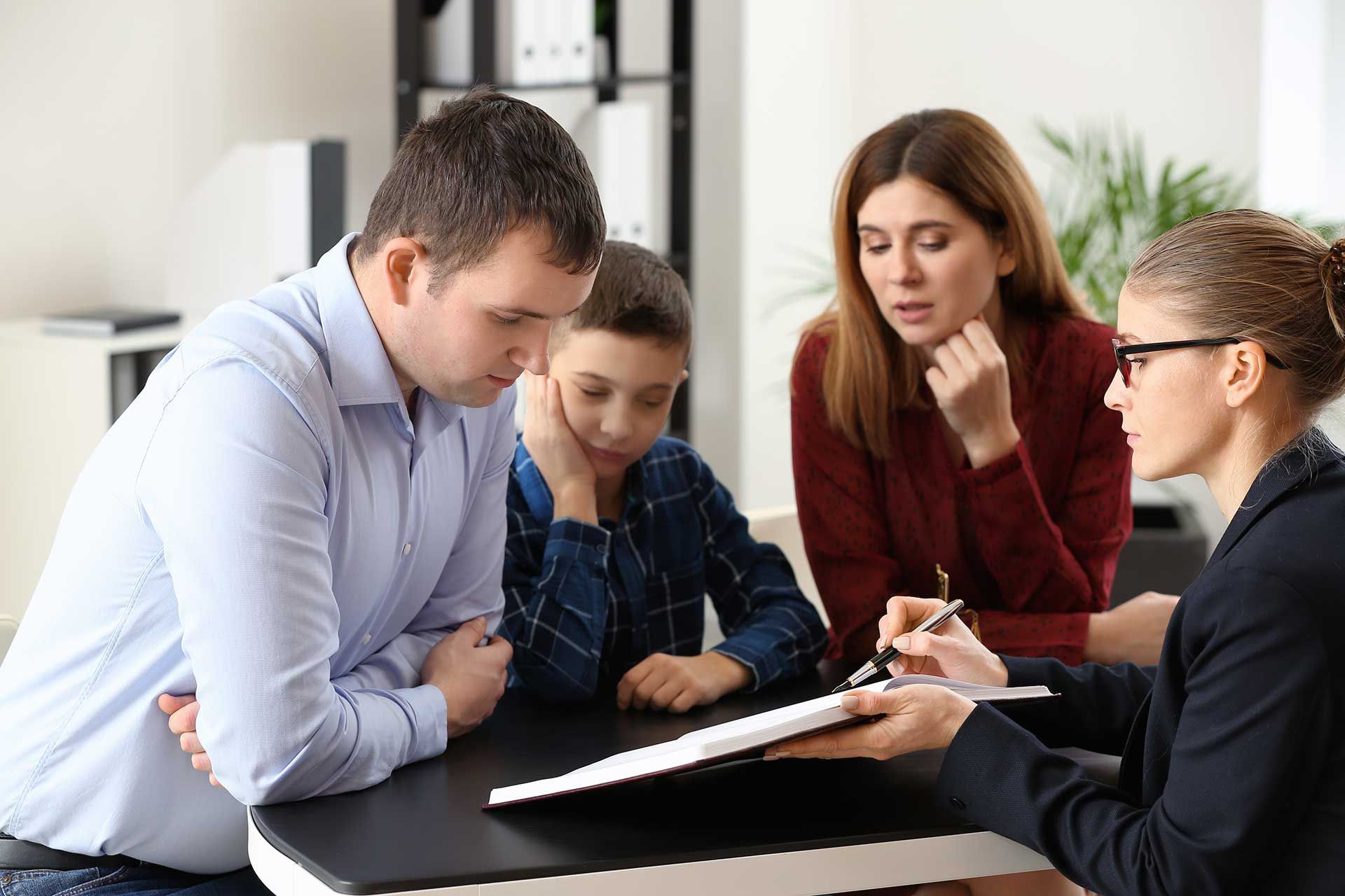 A family is sitting at a table talking to a woman.