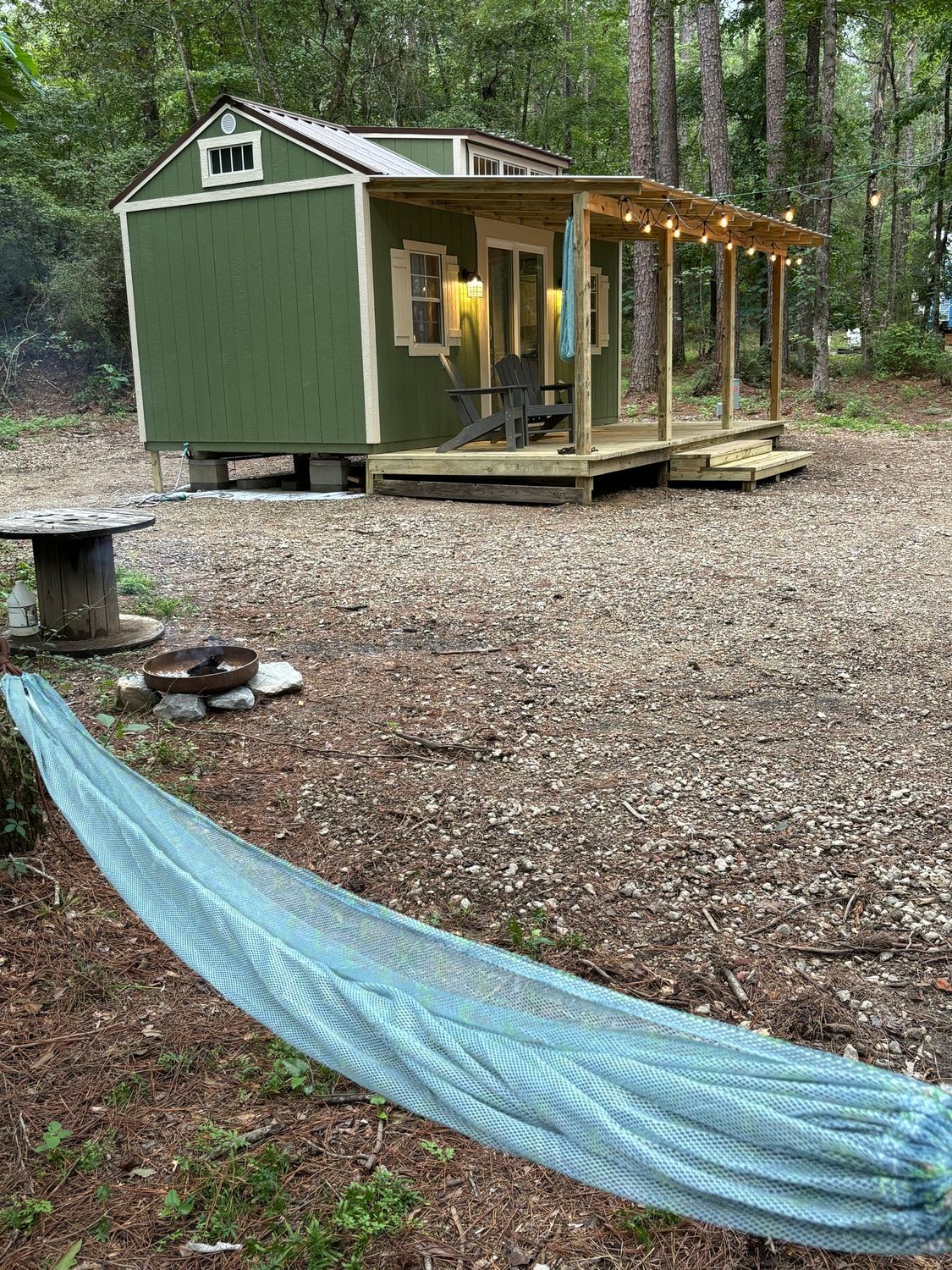A green shed with a porch and a hammock in front of it.