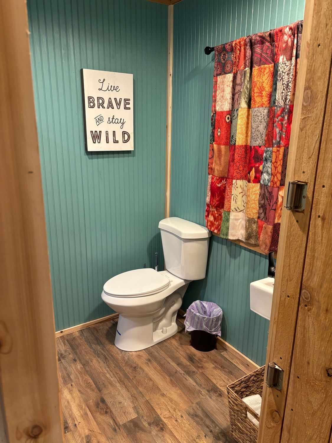 A bathroom with a toilet , sink and a sign that says `` live brave wild ''.