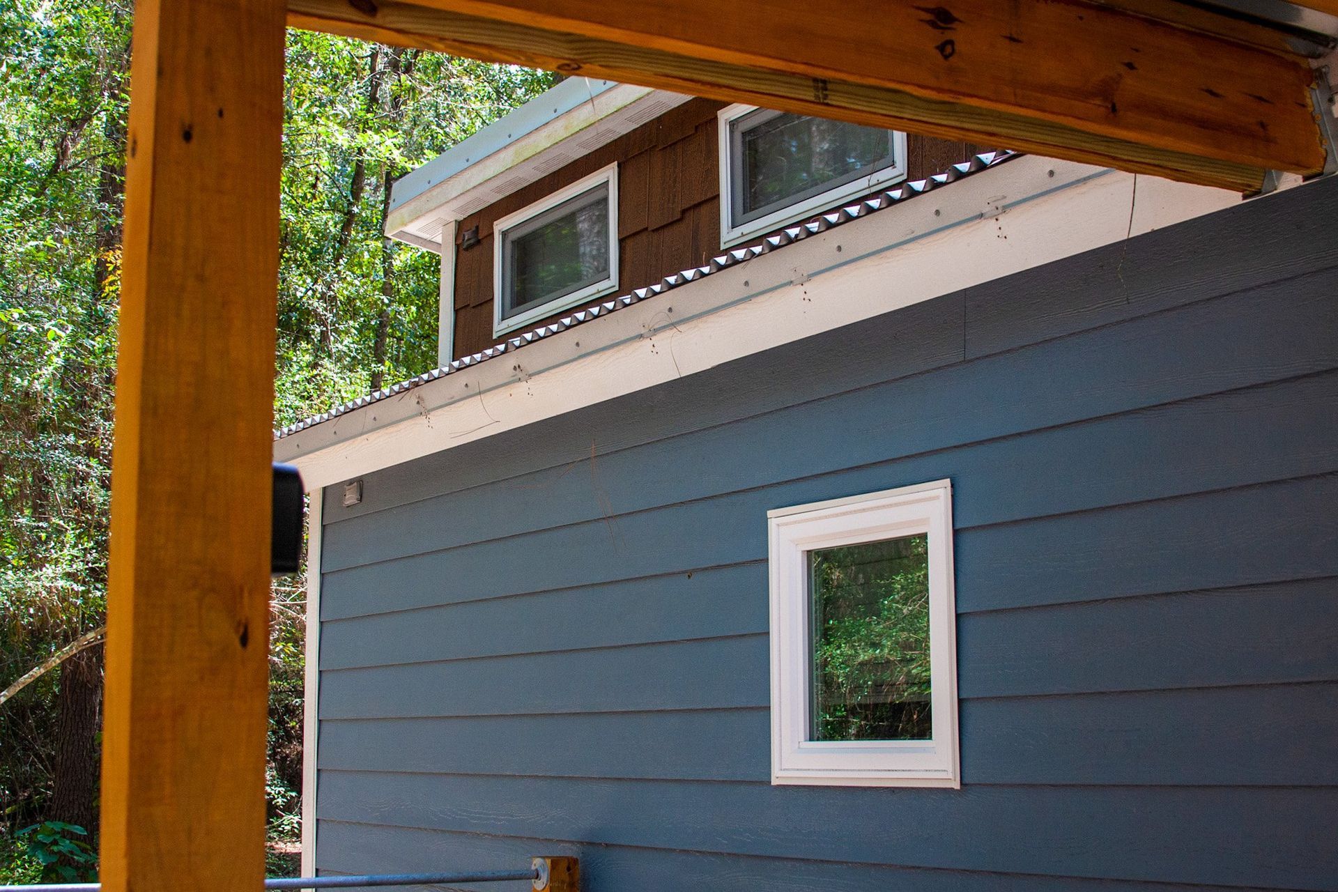 A blue house with a brown roof and a white window.