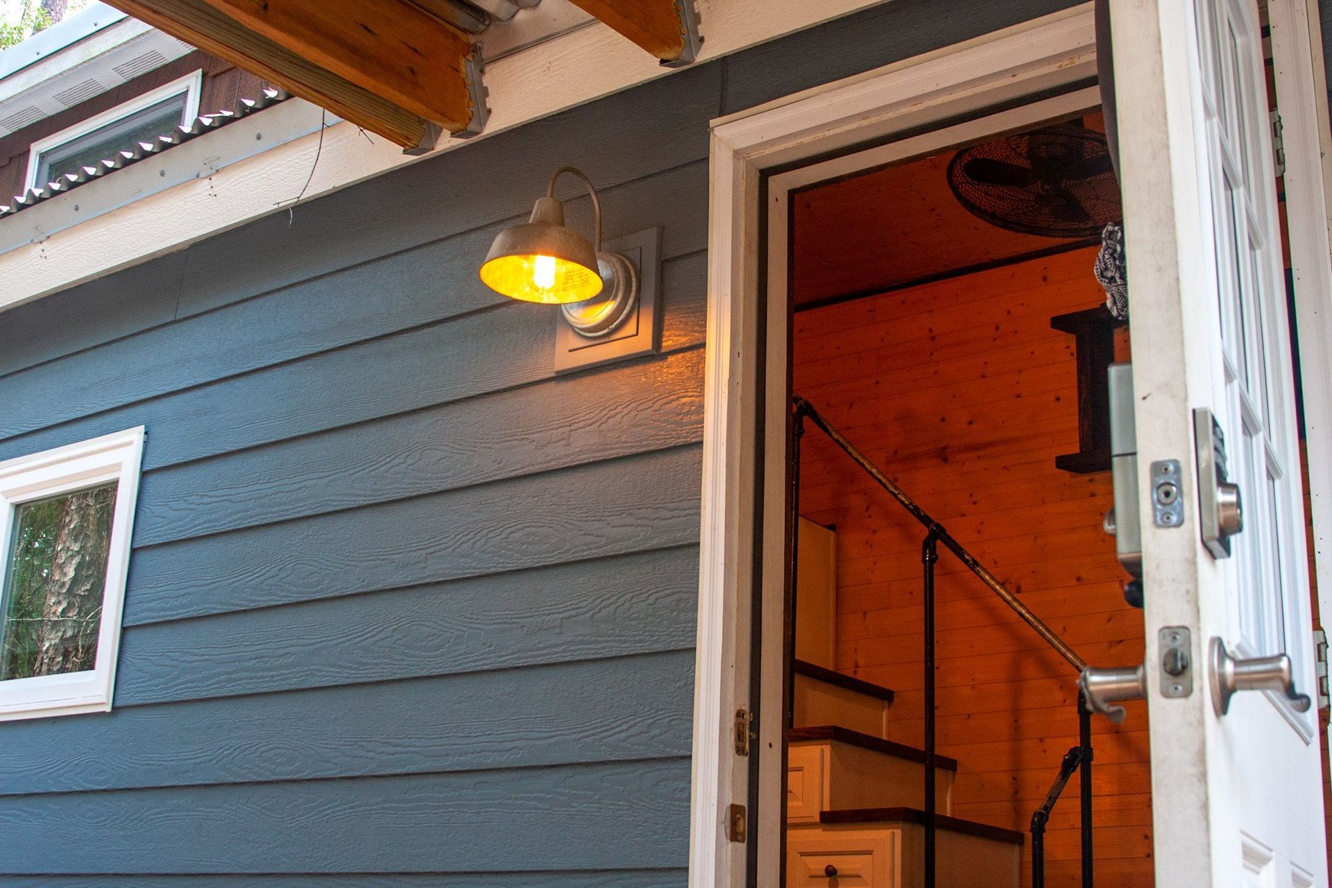 The door is open to a small house with stairs and a light on the wall.