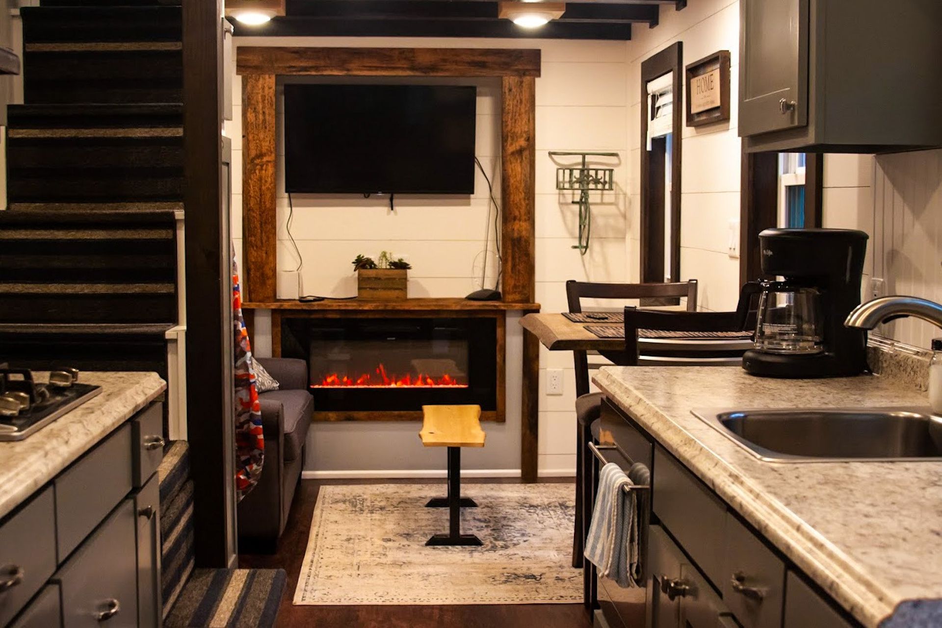 A kitchen and living room in a small house with a fireplace and a flat screen tv.
