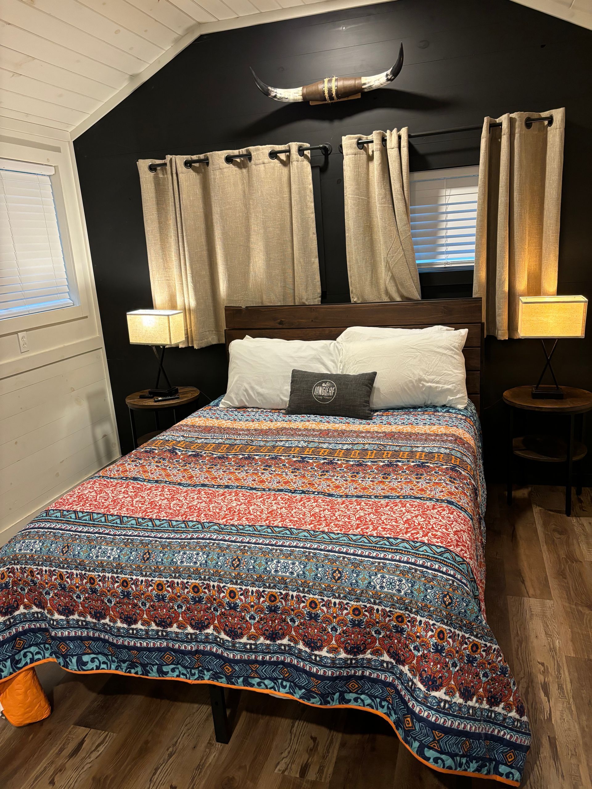A bedroom with a bed , lamps , curtains and a horn on the wall.