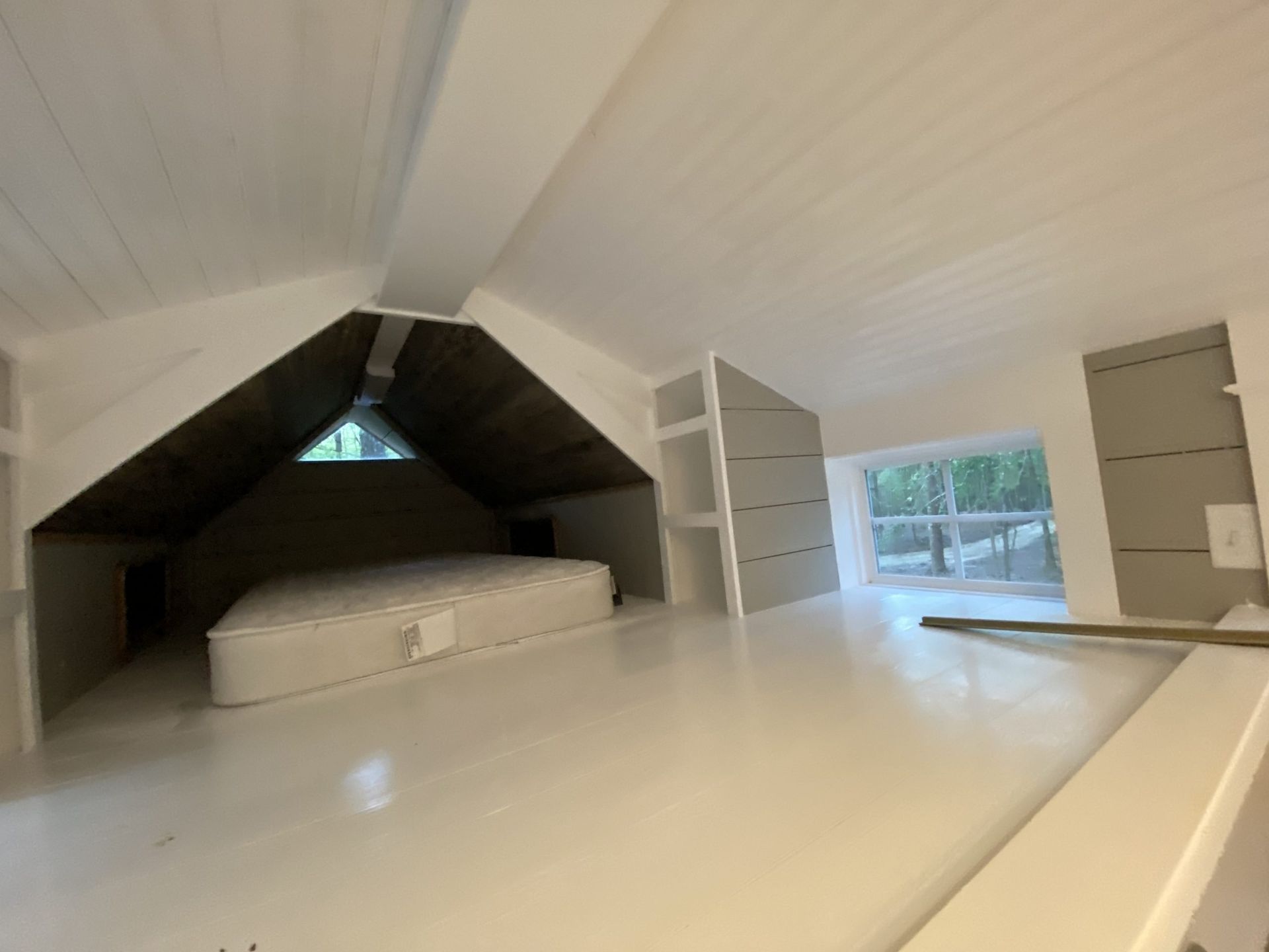 There is a bed in the attic with a window.