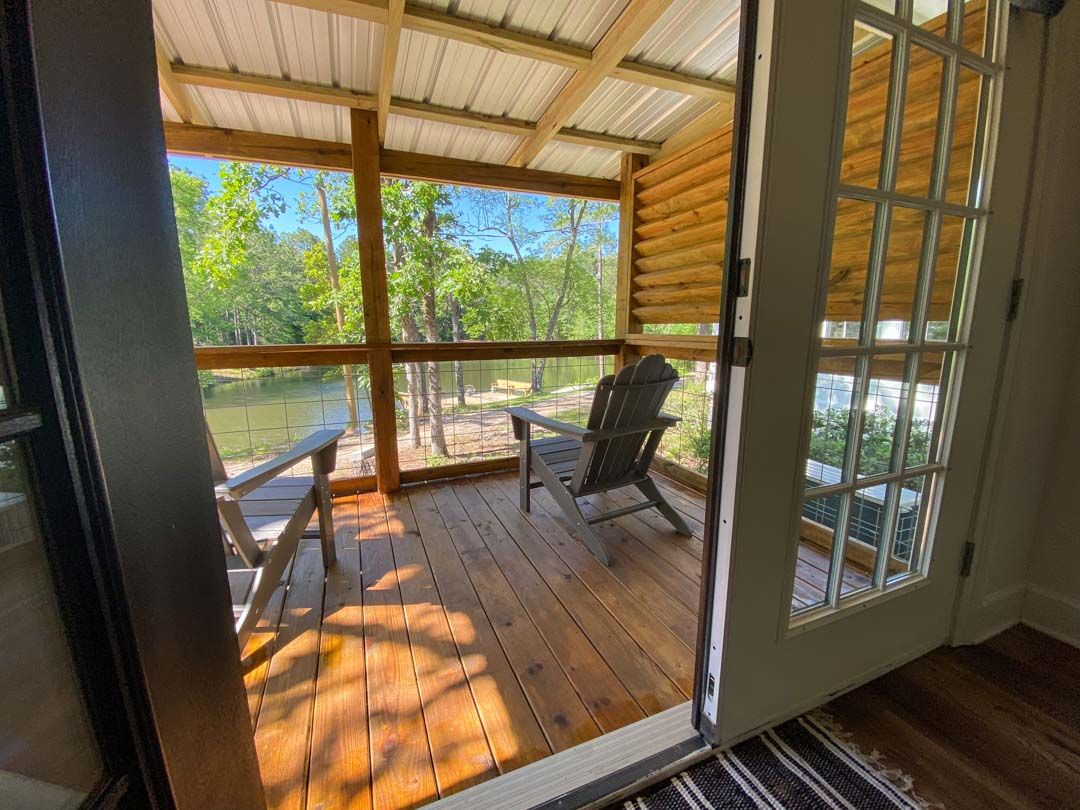 A screened in porch with chairs and a view of a lake.