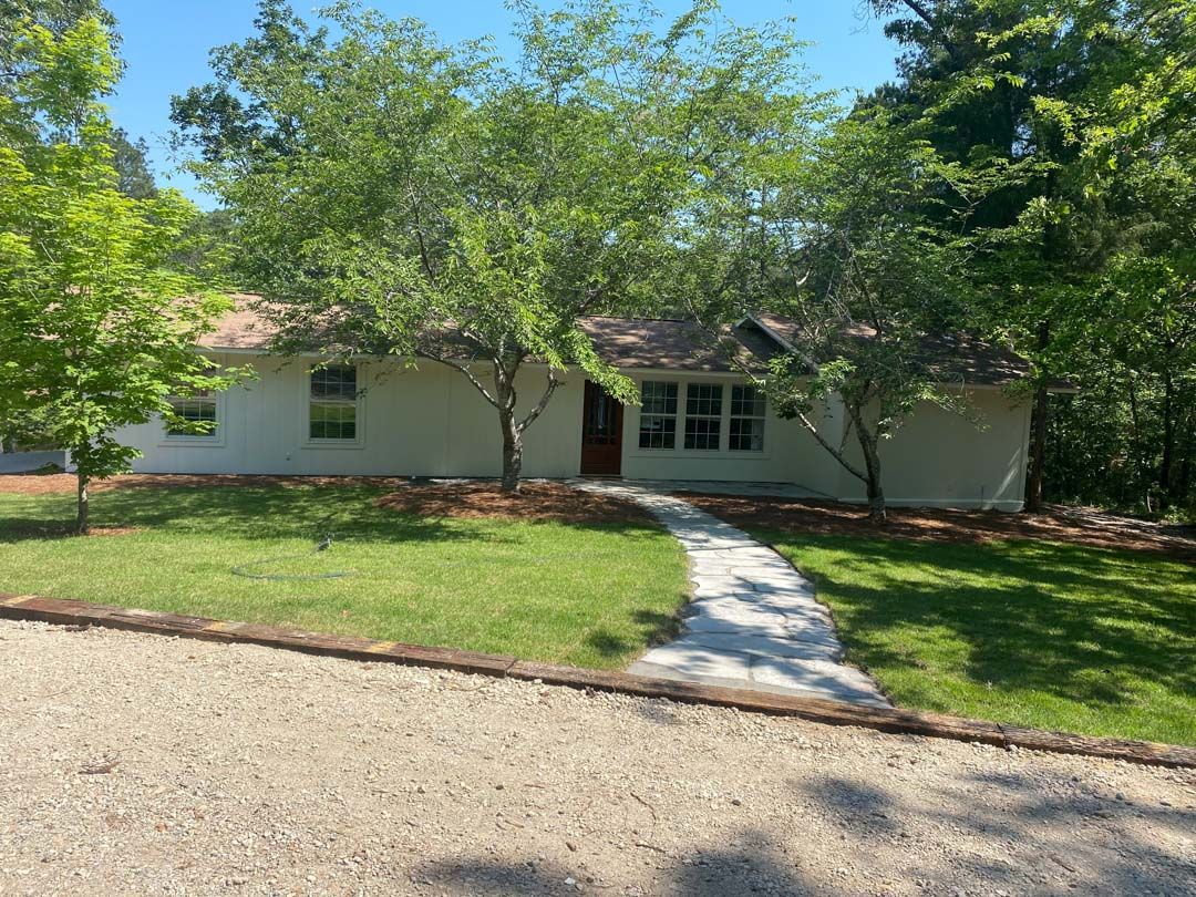 A white house with a walkway leading to it is surrounded by trees and grass.