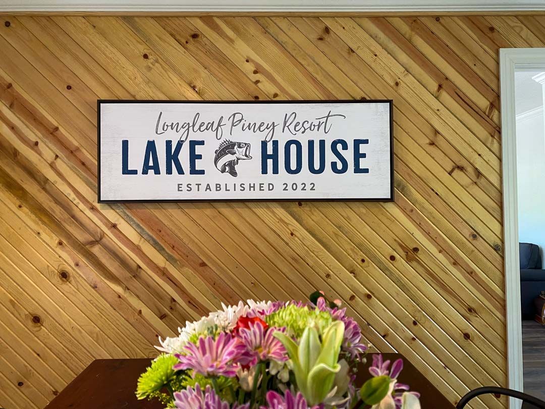 A sign that says lake house is hanging on a wooden wall.