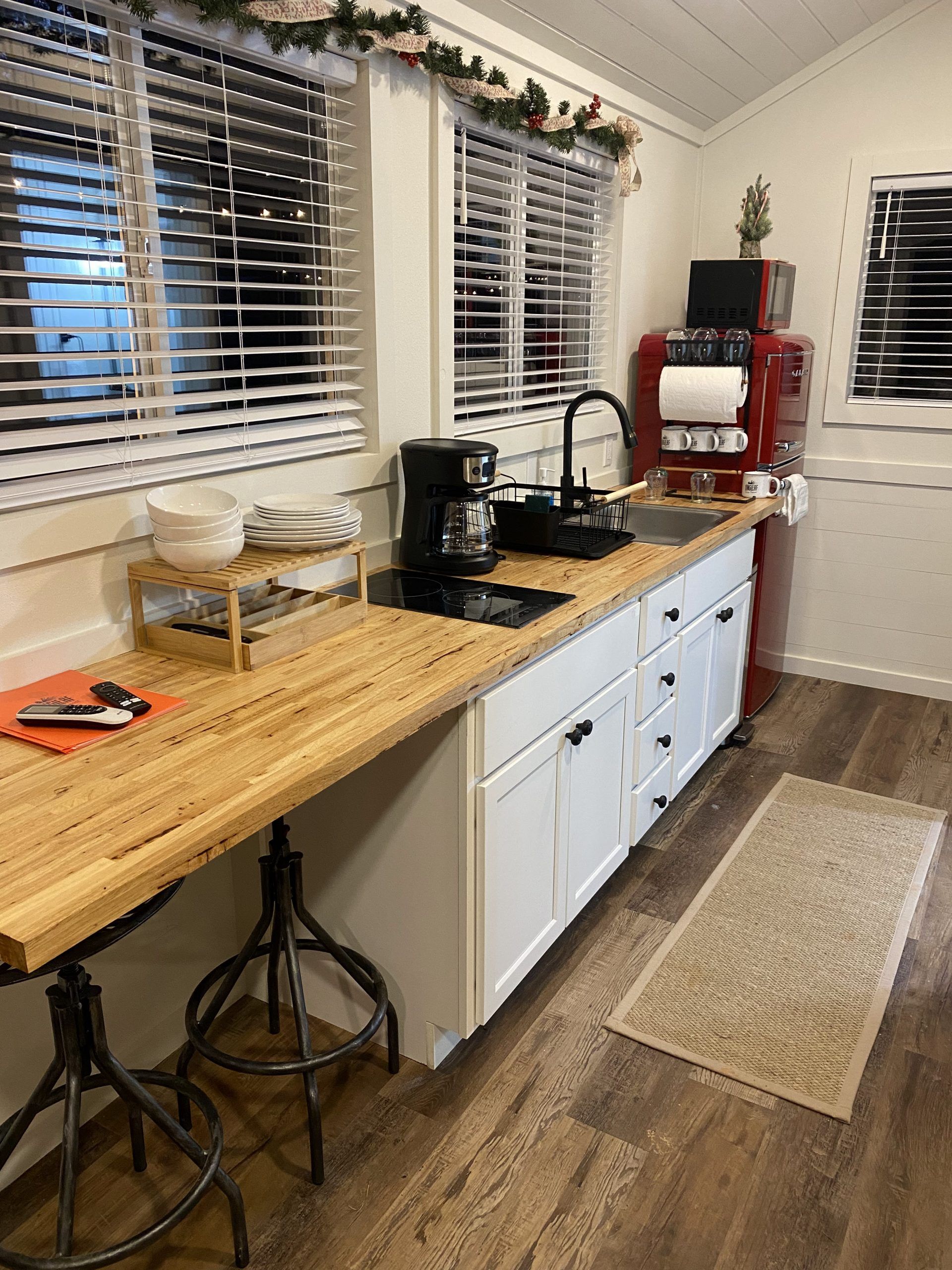 A kitchen with a wooden counter top , white cabinets , a sink , and a coffee maker.