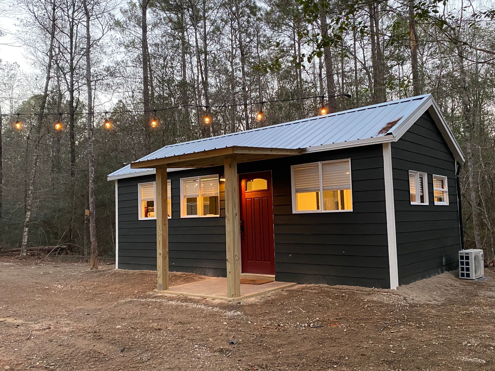A small black house with a red door is in the middle of a forest.