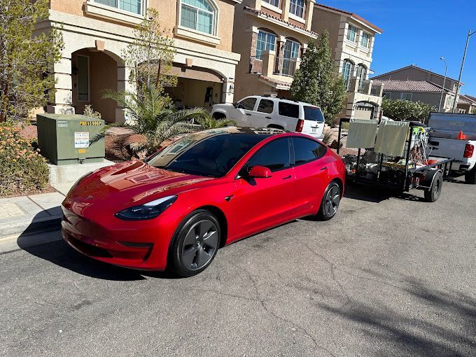 A red tesla model 3 is parked on the side of the road