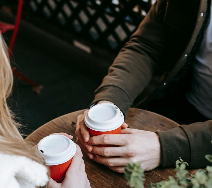 A man and a woman are sitting at a table holding cups of coffee.