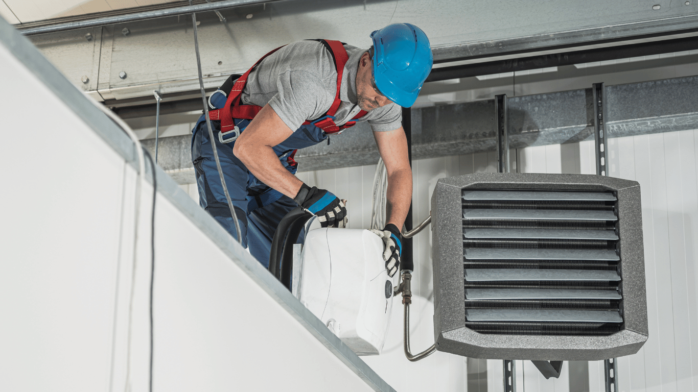 A man is working on a heater on the ceiling of a building, providing gas heater maintenance for reliable warmth.