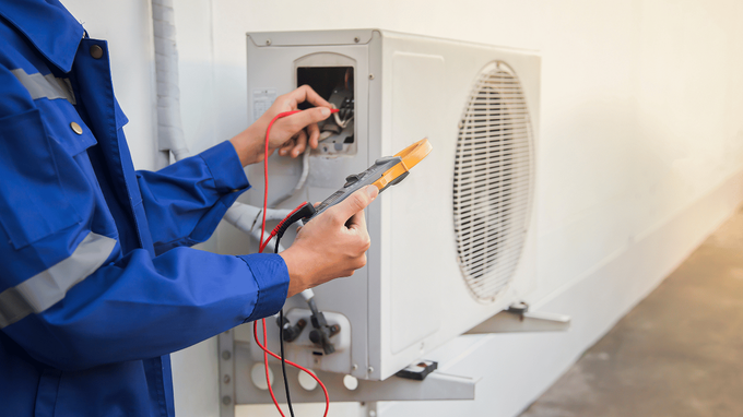 A man is working on an air conditioner with a multimeter, performing residential AC repair to ensure optimal performance.