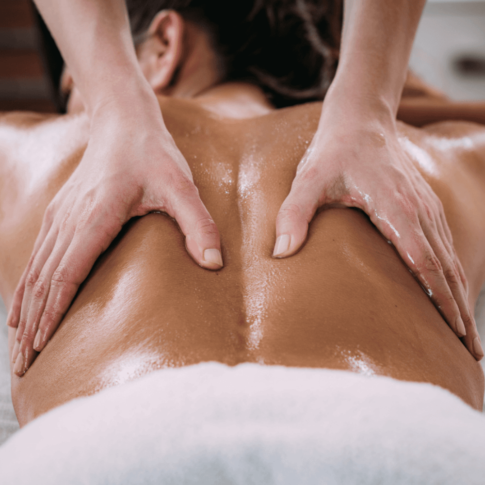 Hands massaging a person's oiled back on a massage table.