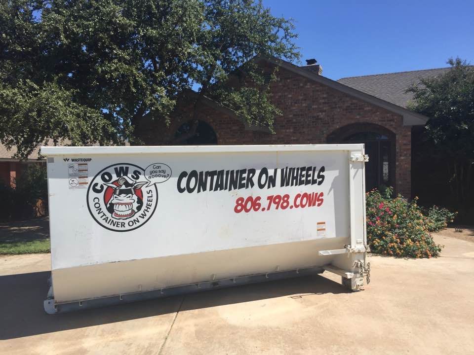 Woman in straw hat smiles, holding wine glass near a lake.