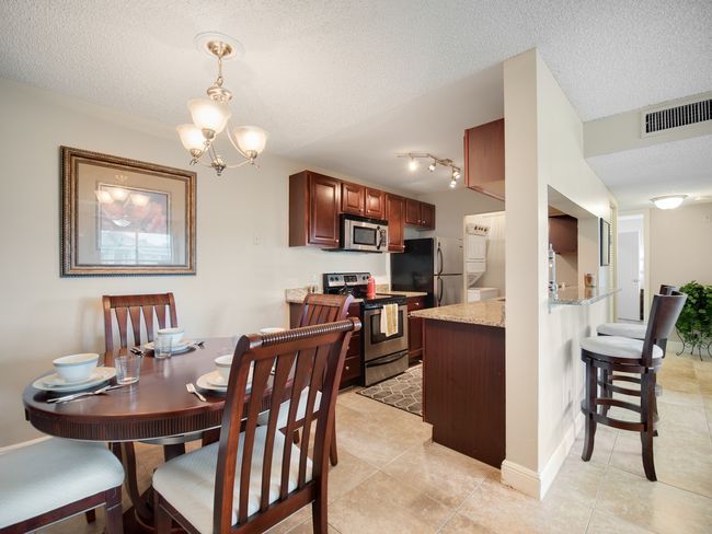 Dining area with round wooden table, chairs, and open kitchen with dark cabinets.