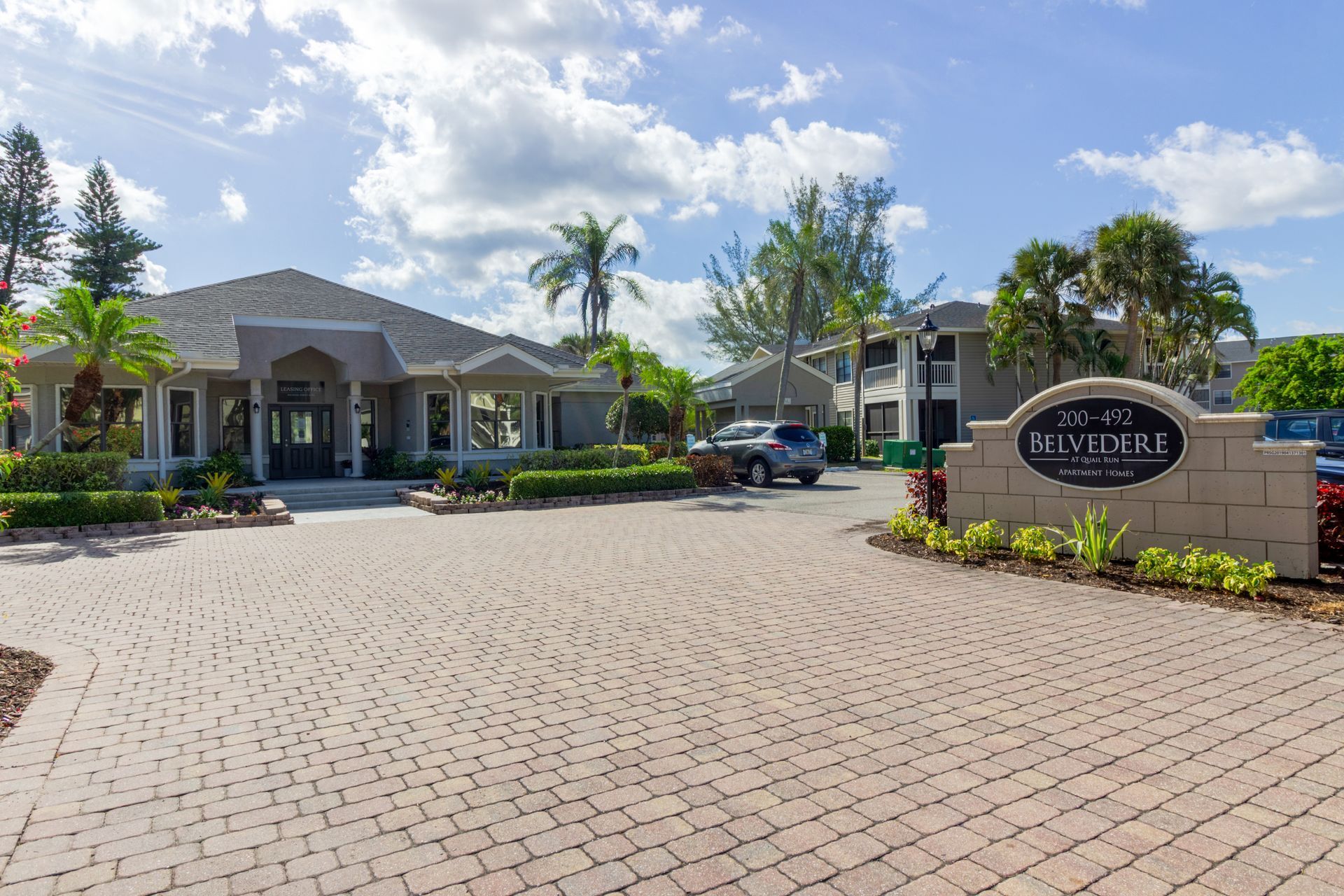 Entrance to The Red-Taire apartment complex with a brick driveway and sign on a sunny day at Belvedere at Quail Run in Naples, FL.