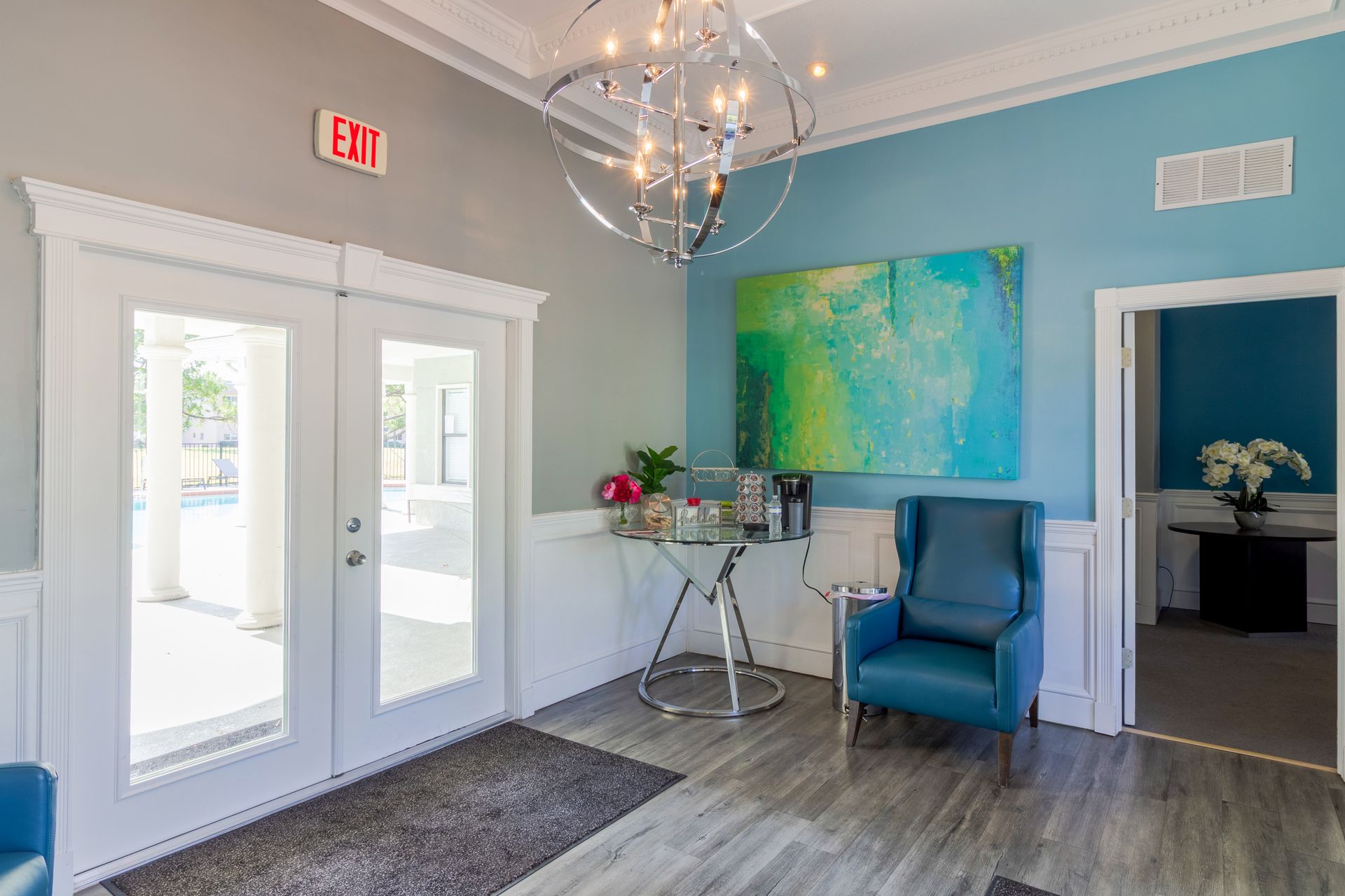 Lobby with teal walls, open double doors to outside, a painting, a chair, and a chandelier at Belvedere at Quail Run in Naples, FL.