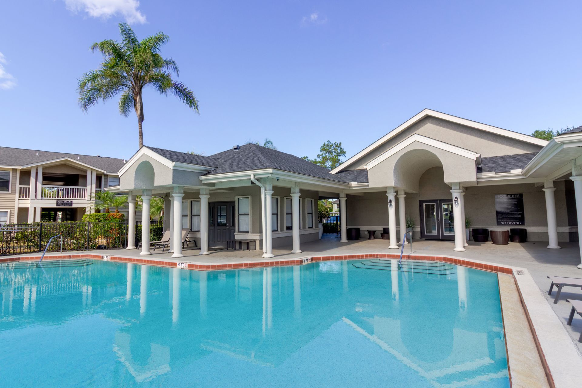 Pool with covered seating area and palm tree under a blue sky at Belvedere at Quail Run in Naples, FL.