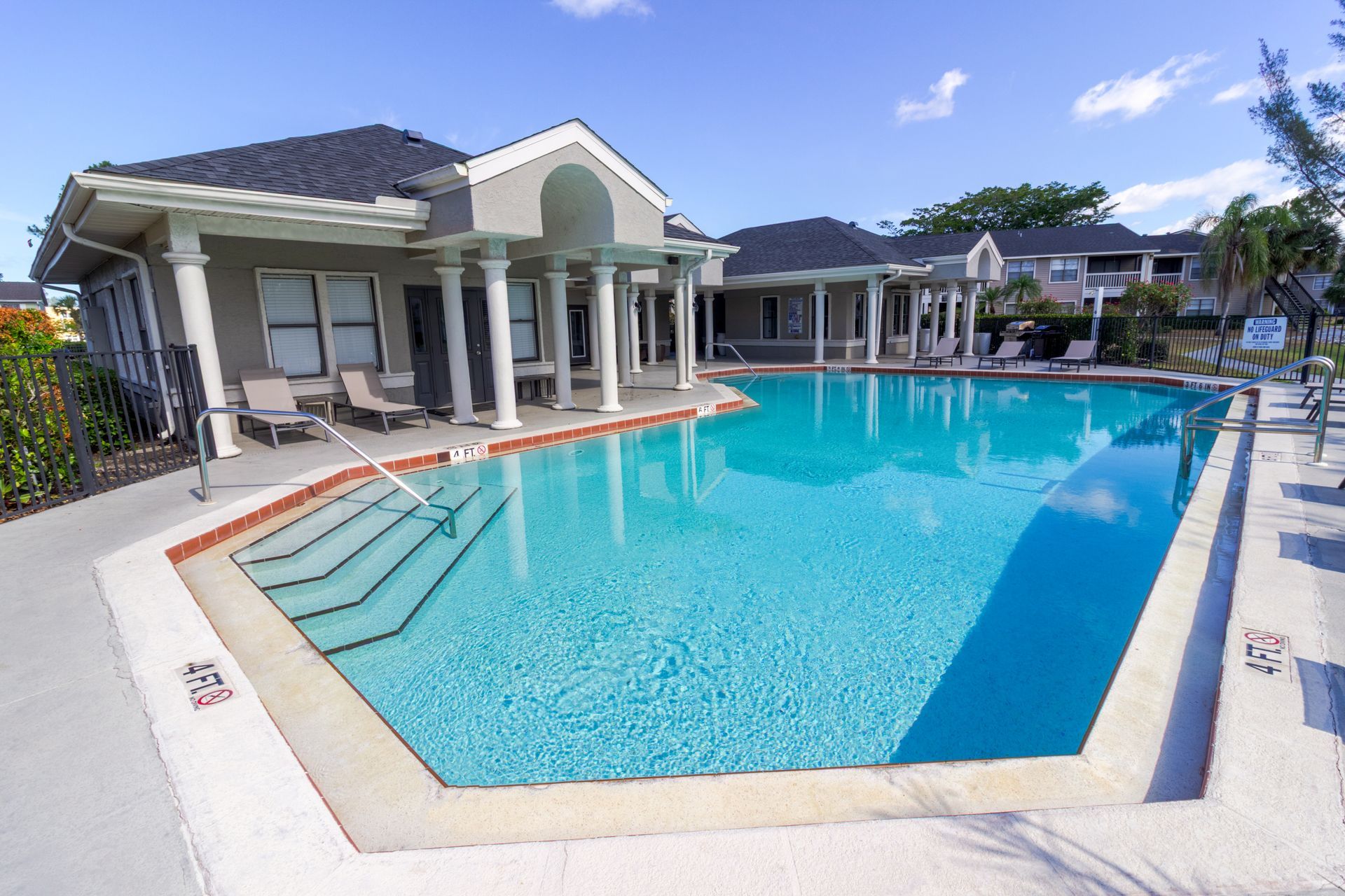 Swimming pool with building, columns, and lounge chairs. Blue water, sunny day at Belvedere at Quail Run in Naples, FL.