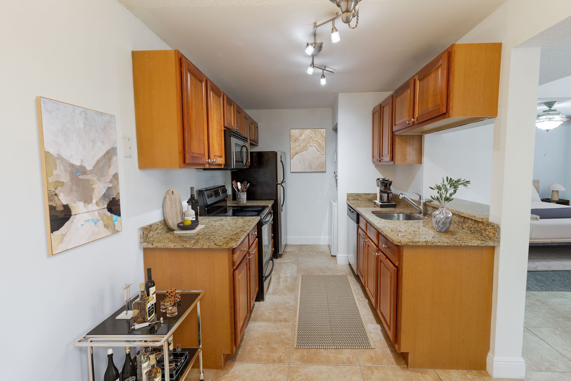 A galley kitchen with light wood cabinets, granite countertops, and a wine cart.