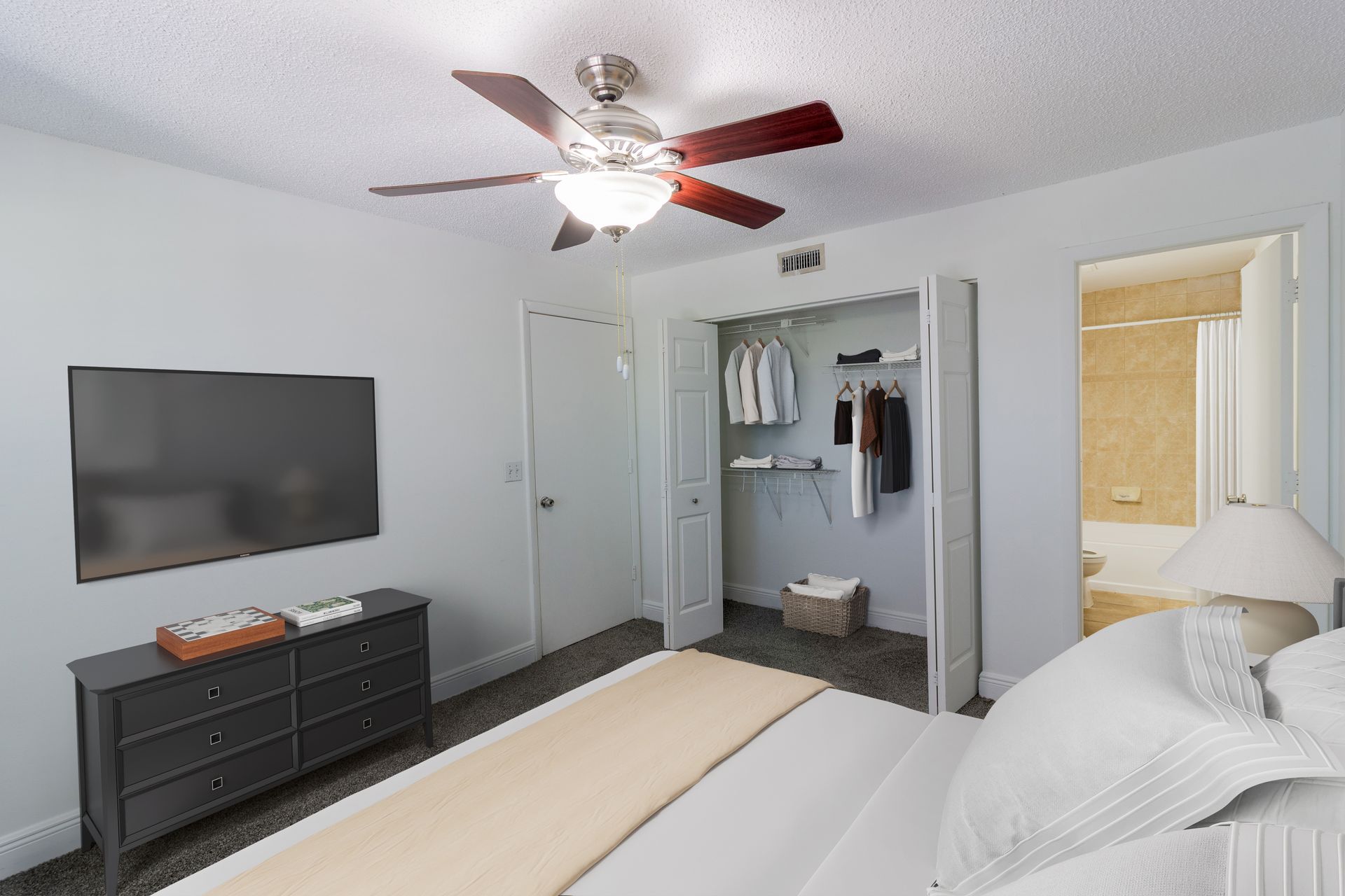 Bedroom with a bed, TV, dresser, open closet, and a doorway to a bathroom.