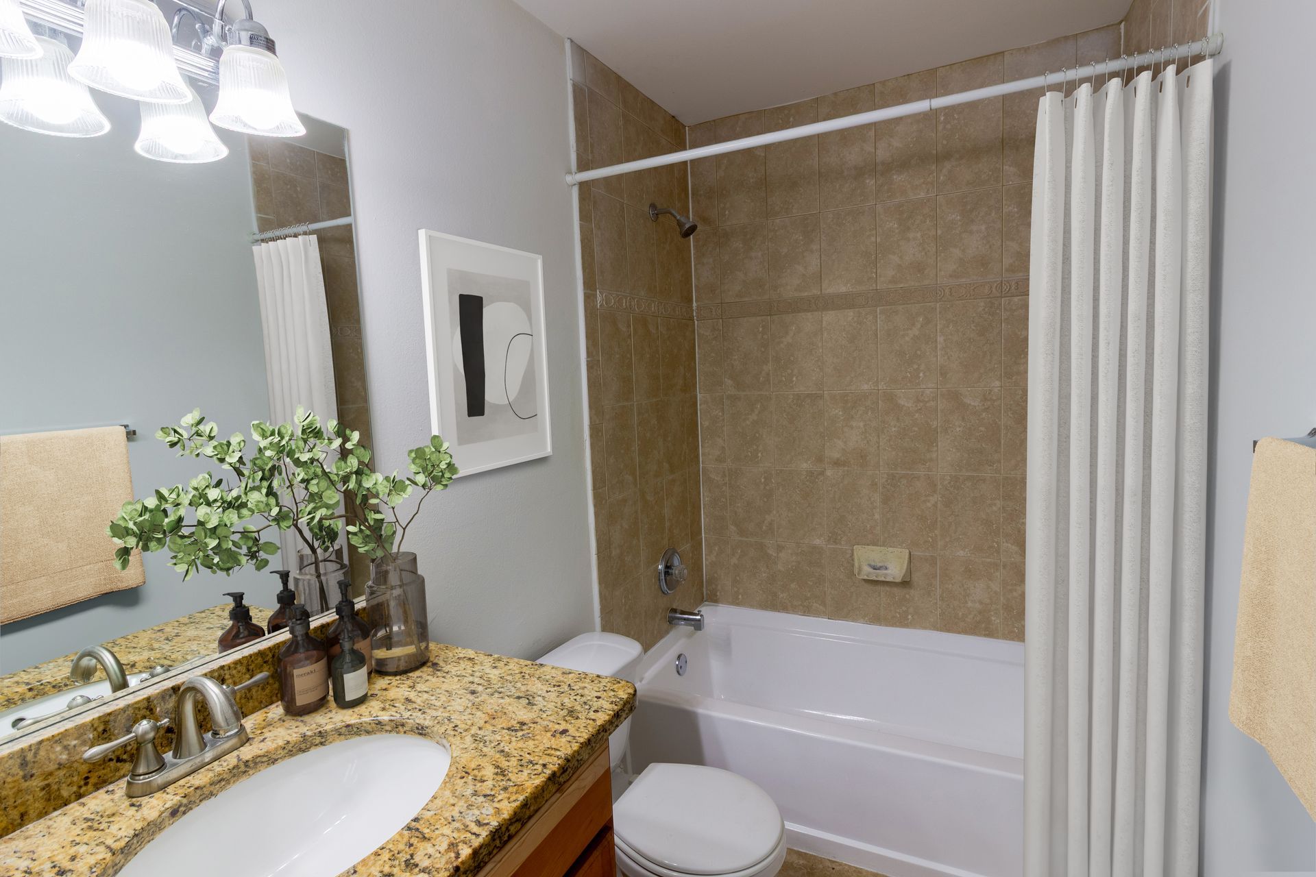 Bathroom with beige tile, white tub, and vanity with a granite countertop.