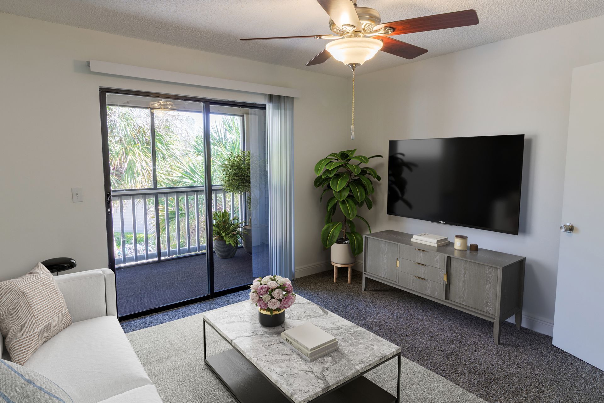 Living room with sliding glass door to balcony, a sofa, TV, and coffee table.