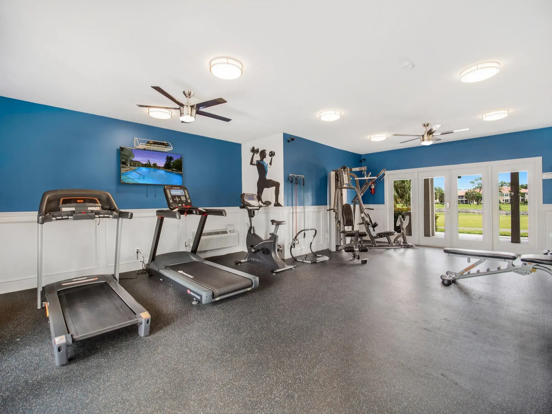 A gym with treadmills , a bike , and a ceiling fan.