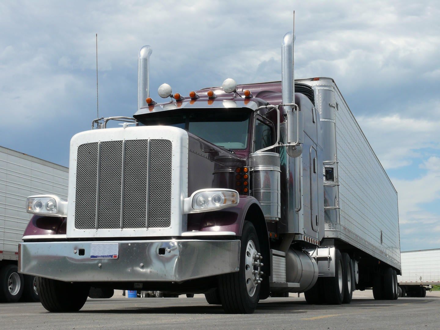 A semi truck is parked in a parking lot next to a trailer.
