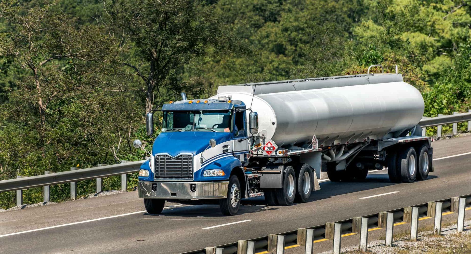 A blue and silver tanker truck is driving down a highway.