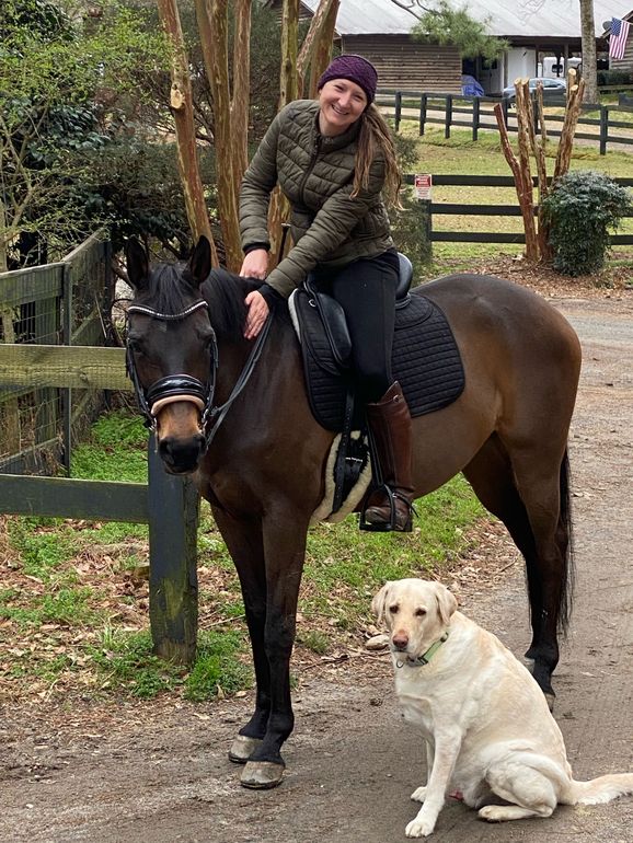 A woman is riding a horse next to a dog.