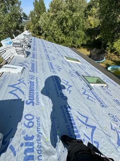 A person is standing on a roof with a roofing material on it.