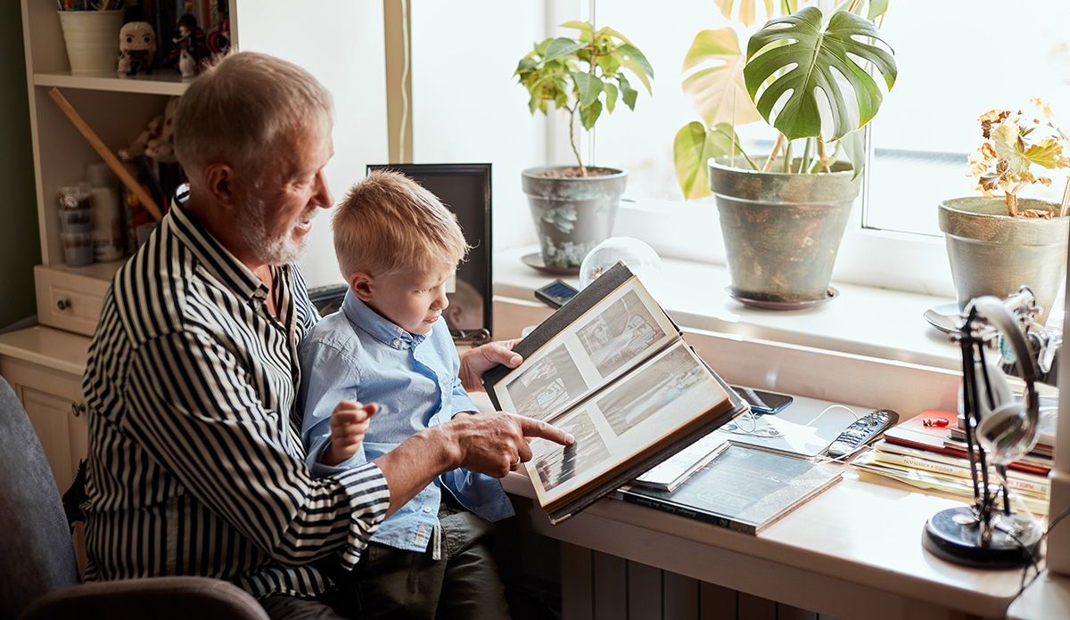 An elderly man is reading a book to a young boy.