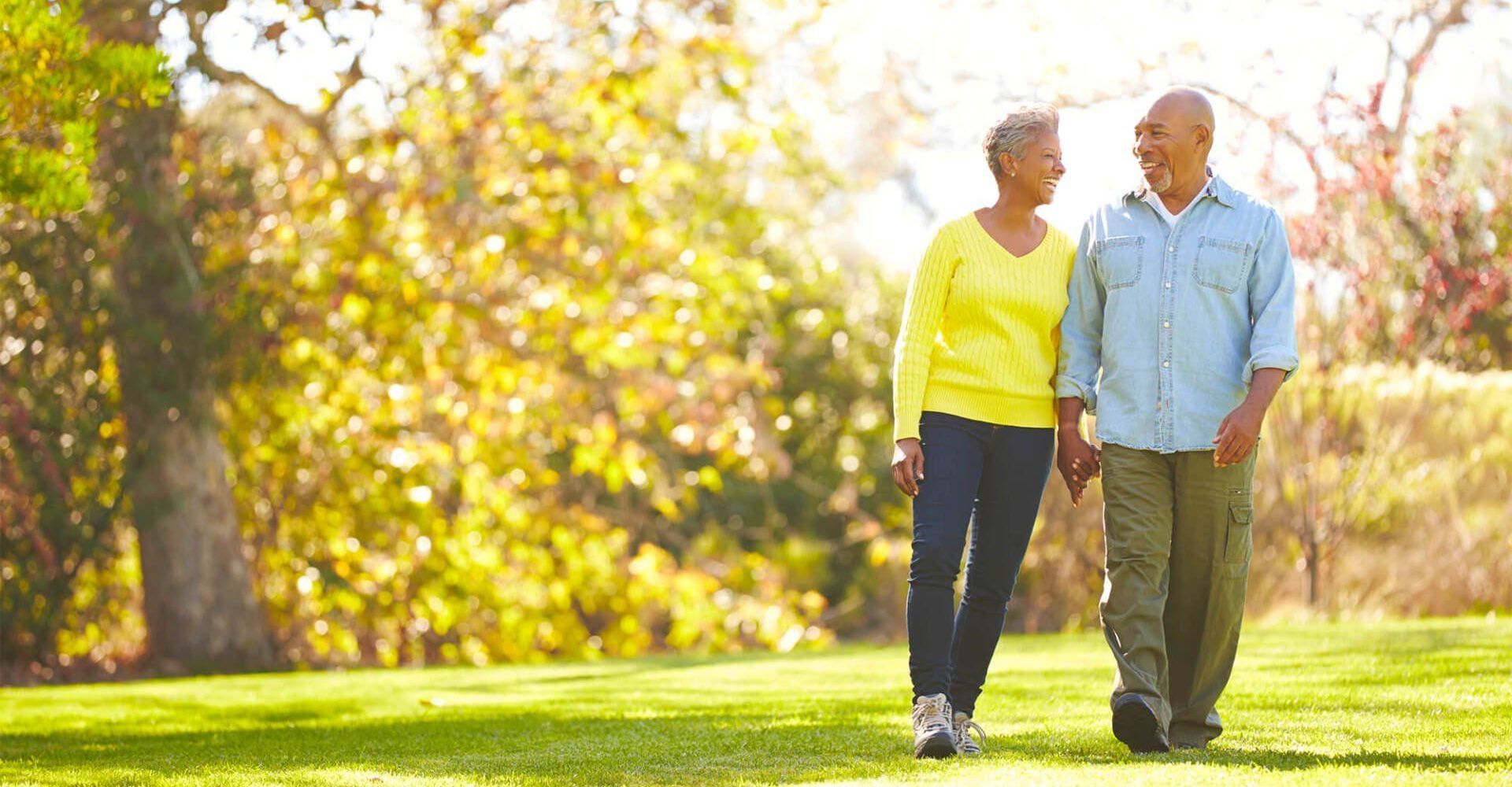 An elderly couple is walking in a park holding hands.