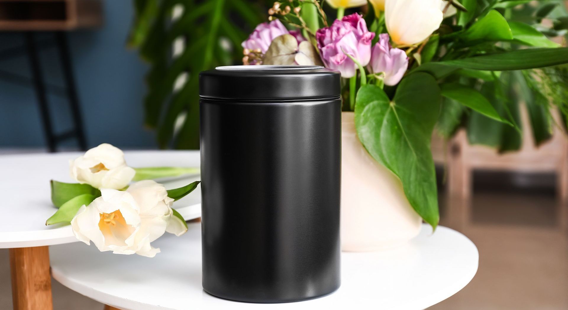 A black can is sitting on a table next to a vase of flowers.