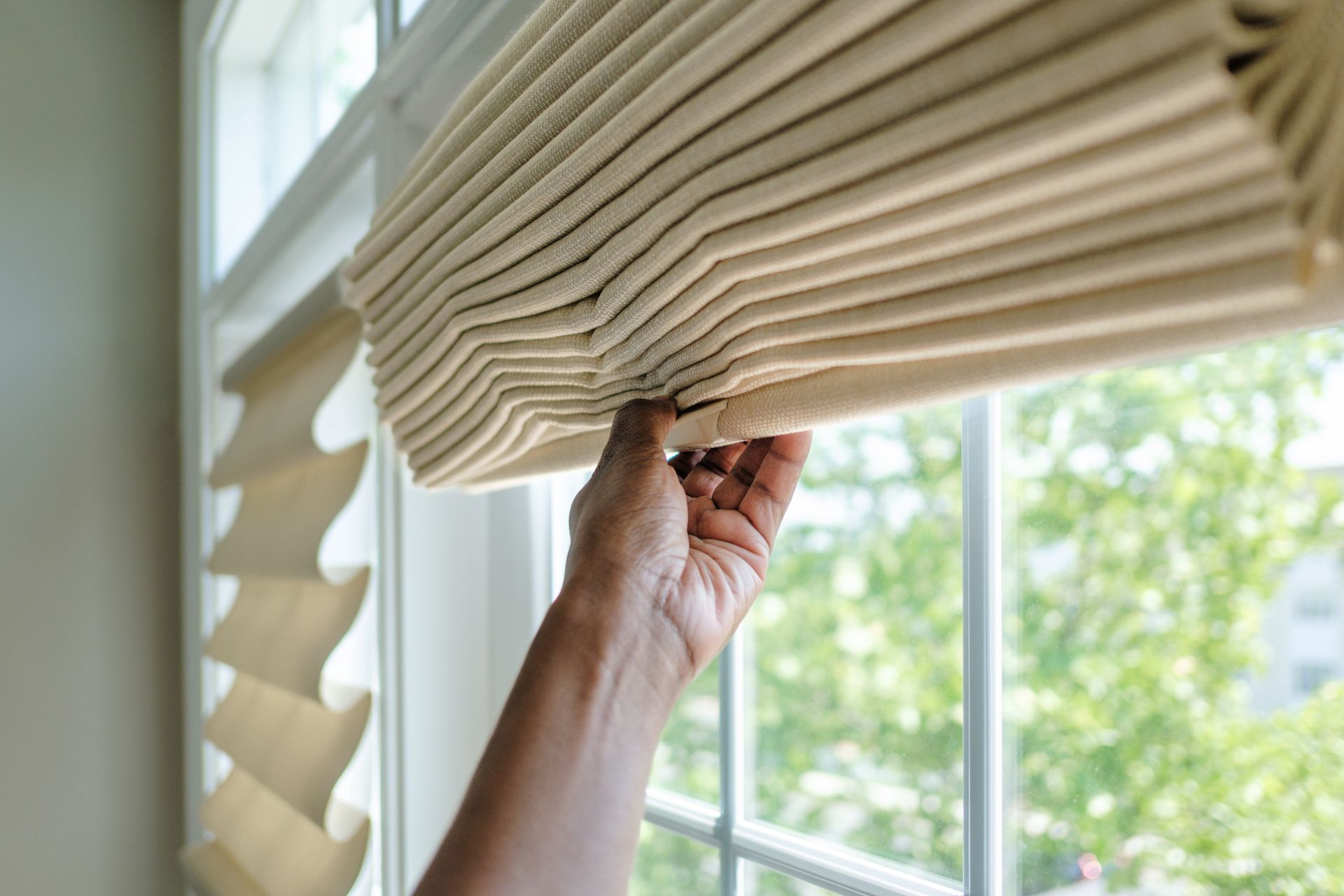 Woman lifting glass window treatments shade for natural light in modern home interior.