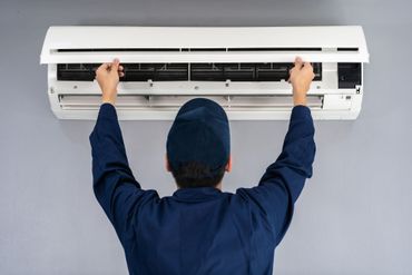 A man in a red shirt is working on an air conditioner outside of a house.