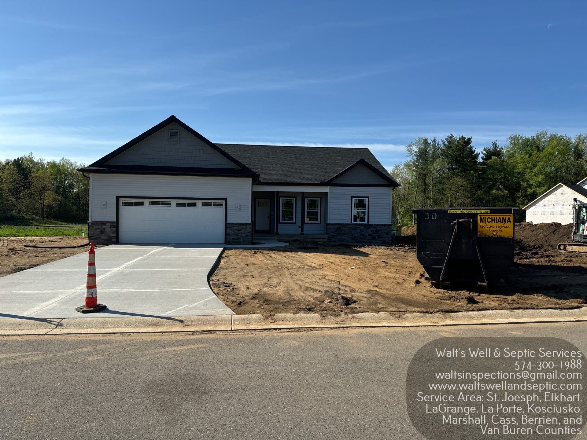 A newly built single-story home with a white exterior, dark roof, and garage, under a clear blue sky.