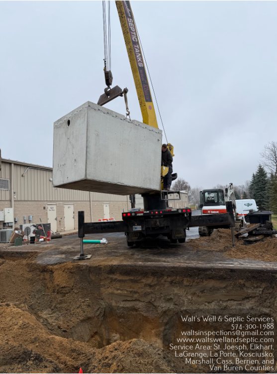 Crane lifting a concrete septic tank over an open excavation site.