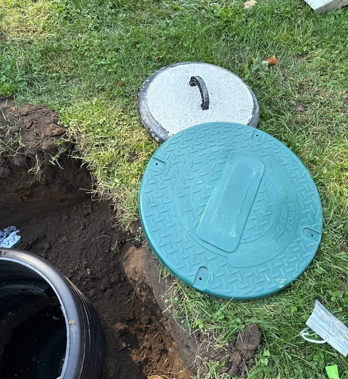 Open septic tank with two covers on the grass near an excavated hole in South Bend, Indiana