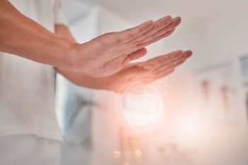 Hands held above a glowing orb, person in white clothing.